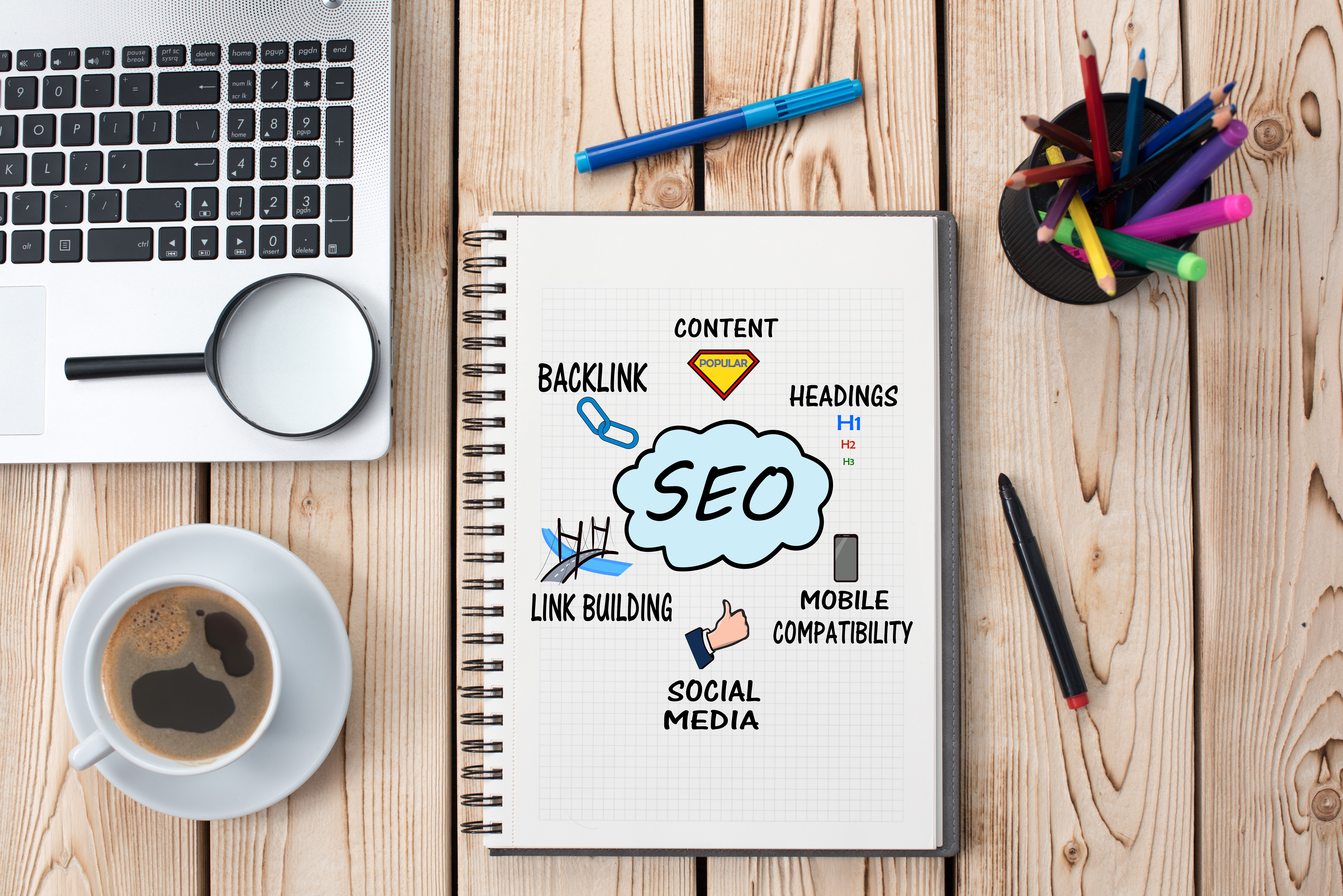 This image shows a photo of a notebook with 'SEO', an abbreviation which stands for 'Search Engine Optimization'. 
                The surrounding illustrations portray concepts related to SEO: Content, Headings, Mobile Compatability, Social Media, Link Building, and Backlink.